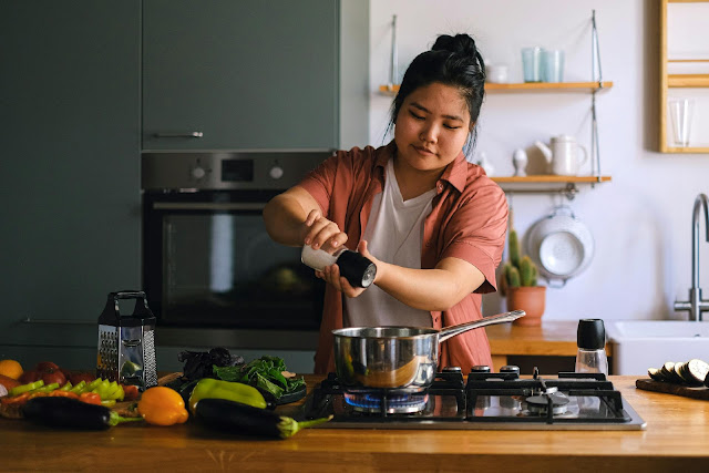 Home cook adding seasoning to a pot while preparing fresh Indian-style food in a modern kitchen