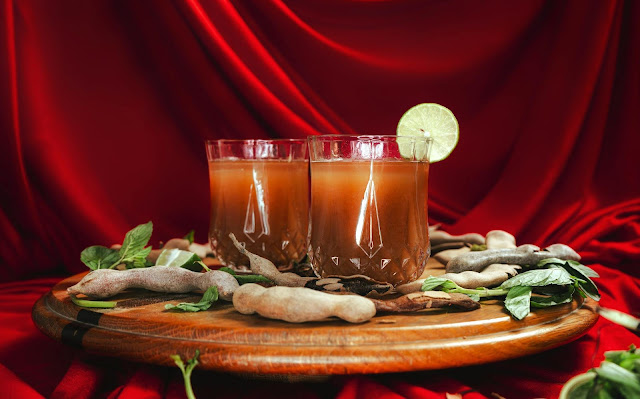 Three glasses of tamarind drink with tamarind pods on a wooden tray