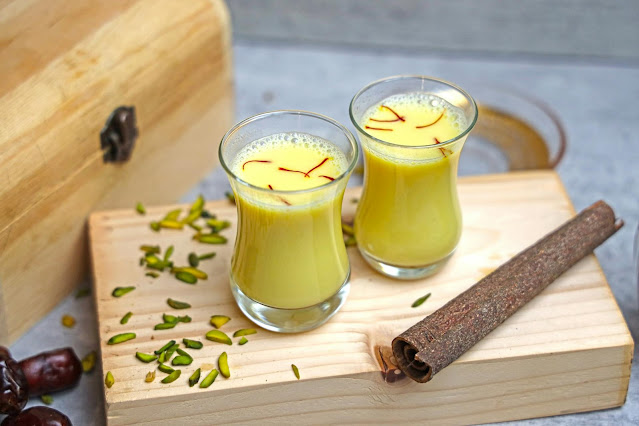 Glasses of saffron milk with pistachios and cinnamon on a wooden table
